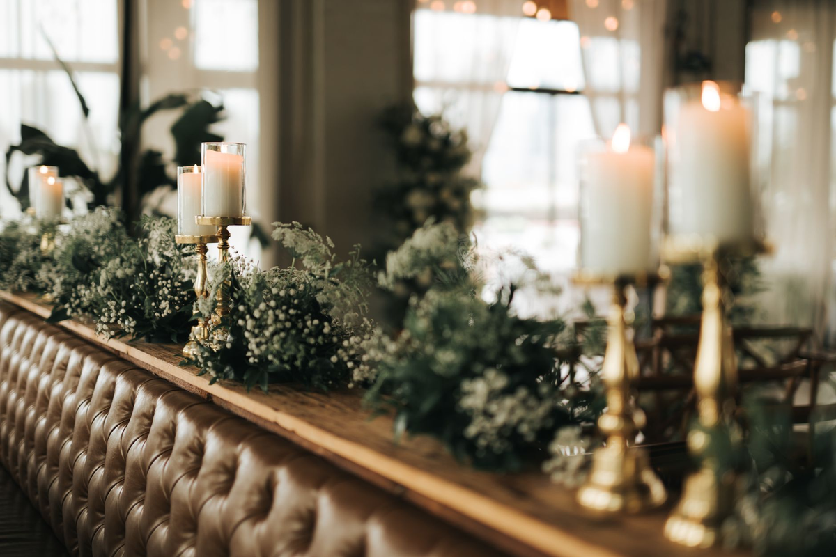 Long dining table dressed with greenery and lanterns under warm string lighting